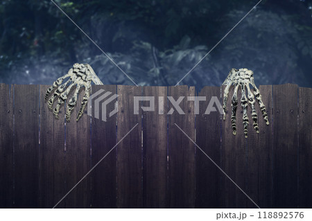 Human skeleton hand rising out of behind wooden fence, with a creepy, dark and scary mood. The skeleton hand appearing to be a devil, evil, satan, zombie or a monster hand 118892576