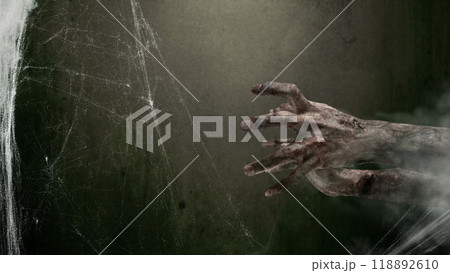 Zombie hands with bloody wound shown in a dark room with a cobweb spider web in the background. The hand appearing to be devil, evil, satan, or monster hands 118892610