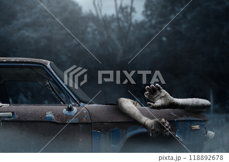 Mummy hands have dirty bandages on them sticking out of on the car hood. The car is old and rusted. Mummy, devil, evil, satan or zombie hands. The scene has dark and creepy Mummy hands have dirty bandages on them sticking out of on the car hood. The car is old and rusted. Mummy, devil, evil, satan or zombie hands. The scene has dark and creepy 118892678