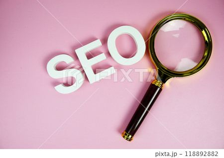 Seo words (Search Engine Optimization) letters with magnifying glass on pink background 118892882