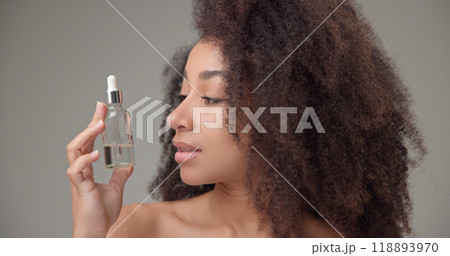 Beauty and healthcare concept - beautiful african american woman with curly afro hairstyle and clean, healthy skin holding a dropper bottle with skin care serum 118893970