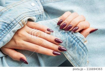 Elegant hands with polished burgundy nails resting on a denim jacket sleeve Elegant hands with polished burgundy nails resting on a denim jacket sleeve 118894363