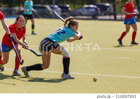 Female attacker hitting the ball in an intense field hockey match on a sunny afternoon Female attacker hitting the ball in an intense field hockey match on a sunny afternoon 118897891
