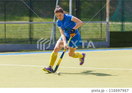 Young female player running with the ball in a field hockey match Young female player running with the ball in a field hockey match 118897987