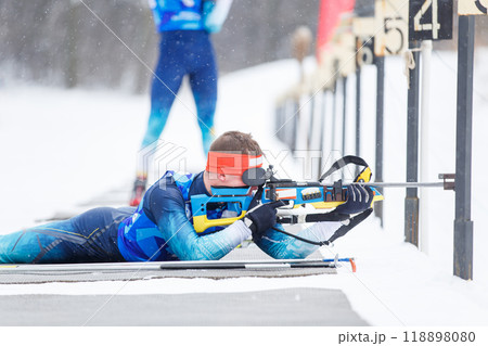 Athlete shooting in prone position at the range in a biathlon competition 118898080