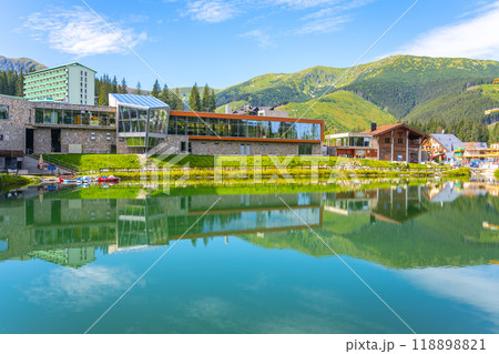 The tranquil waters mirror the scenic beauty of Jasna Ski Resort in the Low Tatras. Vibrant greenery and modern architecture create a picturesque summer landscape for visitors. The tranquil waters mirror the scenic beauty of Jasna Ski Resort in the Low Tatras. Vibrant greenery and modern architecture create a picturesque summer landscape for visitors. 118898821