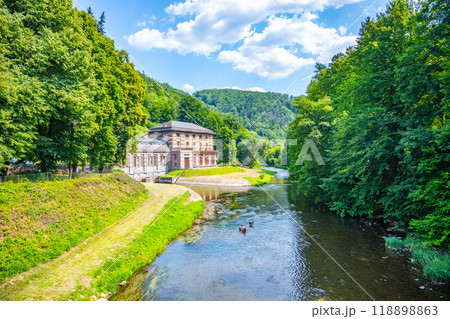 The Spalov Hydroelectric Power Plant sits gracefully by the river, surrounded by lush greenery and hills, bathed in sunlight on a clear day, showcasing nature's harmony with technology. The Spalov Hydroelectric Power Plant sits gracefully by the river, surrounded by lush greenery and hills, bathed in sunlight on a clear day, showcasing nature's harmony with technology. 118898863