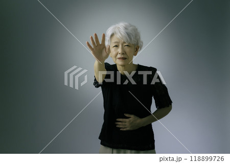 お腹をおさえながら手を伸ばす白髪のシニア女性 118899726