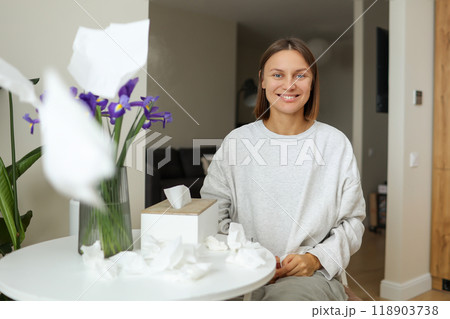 Seasonal allergy free. Happy young woman throws tissues up at home. Healthy life without of runny nose, itching or cough symptoms. Allergen bouquet of iris flowers at vase and used napkins on table. 118903738