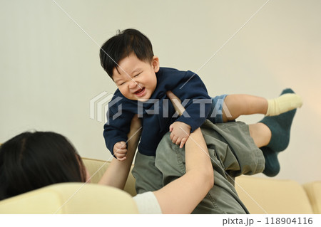 Playful young mother lifting her adorable little baby with her legs while lying on couch at home 118904116