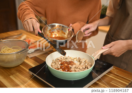 Close up shot of young couple cooking, stirring ingredients in frying pan with wooden spatula Close up shot of young couple cooking, stirring ingredients in frying pan with wooden spatula 118904187