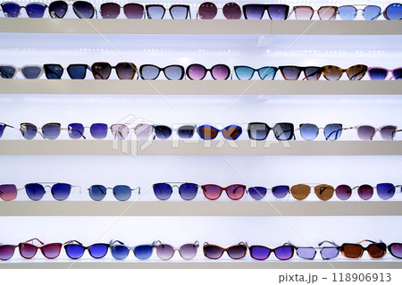 Organized rows of sunglasses, vibrant lenses in different styles, white shelves displaying fashion accessories, retail presentation enhancing shopping ambiance, front view. Organized rows of sunglasses, vibrant lenses in different styles, white shelves displaying fashion accessories, retail presentation enhancing shopping ambiance, front view. 118906913