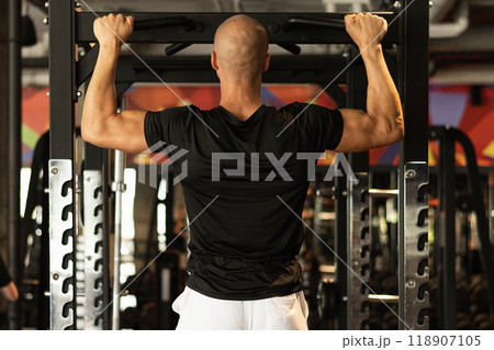 Sports man make pull ups on horizontal bar at gym. Workout. Rear view. 118907105