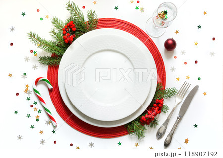 Christmas table setting with vintage dishware, silverware and red decorations on white background. Top view. Christmas table setting with vintage dishware, silverware and red decorations on white background. Top view. 118907192