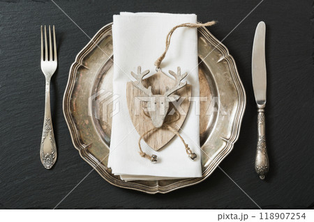 Christmas table setting with vintage dishware, silverware and deer decorations. Top view. Christmas table setting with vintage dishware, silverware and deer decorations. Top view. 118907254