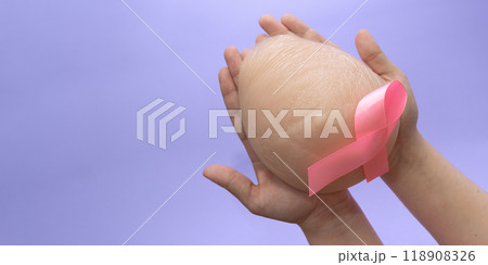 Silicone breast prosthesis on woman hands and Pink Ribbon. Breast Cancer Concept. Copy space Silicone breast prosthesis on woman hands and Pink Ribbon. Breast Cancer Concept. Copy space 118908326