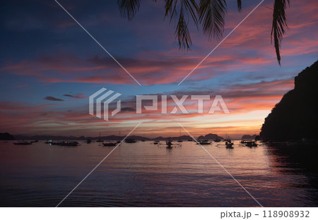 Sunset view over calm waters with boats anchored near the shoreline in a tropical location. El NIdo, Palawan. Sunset view over calm waters with boats anchored near the shoreline in a tropical location. El NIdo, Palawan. 118908932