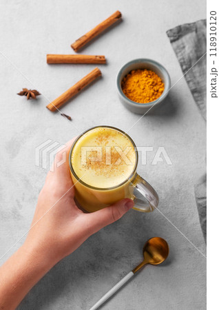 Hand holding turmeric golden milk latte with spices and honey. Detox, immunity boosting drink 118910120