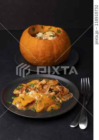 Whole baked pumpkin with tiger prawns, melted cheese and tomatoes. Traditional dish of Brazil, home cooking. Selective focus, close-up, black background. Whole baked pumpkin with tiger prawns, melted cheese and tomatoes. Traditional dish of Brazil, home cooking. Selective focus, close-up, black background. 118910732