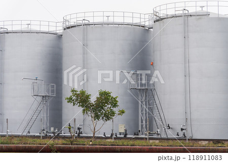 A series of large industrial storage tanks with ladders and piping positioned beside each other, highlighting their significance in manufacturing processes A series of large industrial storage tanks with ladders and piping positioned beside each other, highlighting their significance in manufacturing processes 118911083