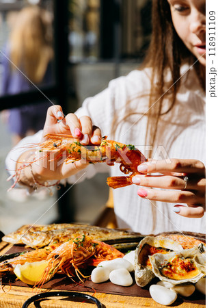 Young woman peeling shrimp at seafood restaurant, perfect for food lifestyle and dining out content 118911109