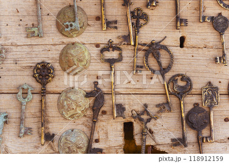 A collection of old and rusted keys are hanging on a wooden wall A collection of old and rusted keys are hanging on a wooden wall 118912159