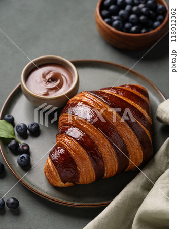 Fresh croissant with chocolate and blueberries on a dark plate on a green background close up. 118912362