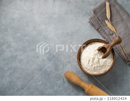 Wheat flour in a wooden bowl with a scoop and rolling pin on a blue background.  118912424