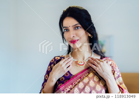 Dressed in beautiful saree, Indian woman delicately putting traditional jewellery getting ready for an ethnic festive celebration. Indian culture and ritual holidays in modern life. Selective focus. 118913049