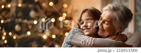 The living room, filled with warmth, shows a grandmother and granddaughter sharing a tender hug next to an elegantly decorated Christmas tree, banner 118913360