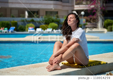 Mediterranean Bliss: Young Woman Relaxing Poolside at Luxurious Resort Under Swaying Palm Trees on Summer Vacation. Serene Summer Getaway: 30-Year-Old Female Sunbathing by Infinity Pool in Idyllic Mediterranean Bliss: Young Woman Relaxing Poolside at Luxurious Resort Under Swaying Palm Trees on Summer Vacation. Serene Summer Getaway: 30-Year-Old Female Sunbathing by Infinity Pool in Idyllic 118914259