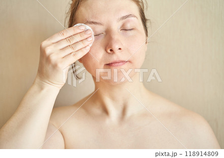 Woman cleansing face with cotton pad for natural skincare routine at home 118914809