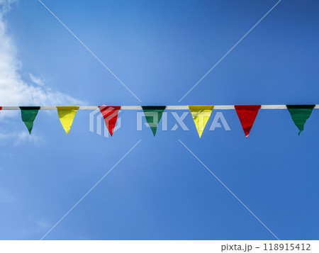 Multicolored garlands or flag flutter in the wind on a summer sunny day with a blue sky with clouds. Multicolored garlands or flag flutter in the wind on a summer sunny day with a blue sky with clouds. 118915412