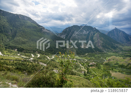 Landscape with mountains, road and fields with trees, flowers on a cloudy summer day after rain 118915837