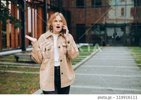 Angry woman on cell phone walking outside building. Frustrated woman talking on phone. Summer time. Negative people emotion 118916111