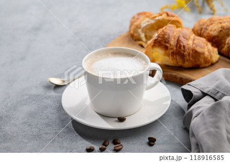 A cup of aromatic cappuccino coffee and fresh croissants on a blue background with coffee beans A cup of aromatic cappuccino coffee and fresh croissants on a blue background with coffee beans 118916585