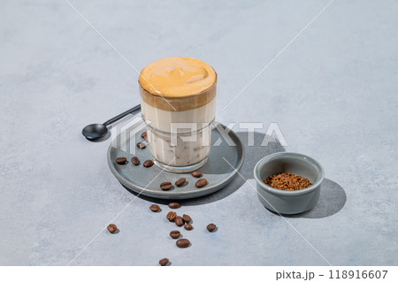 Dalgona coffee. Whipped instant coffee in a glass on a plate with coffee beans on a blue background. 118916607
