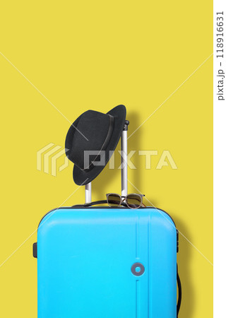 Blue suitcase and black hat on a yellow background. Blue suitcase and black hat on a yellow background. 118916631