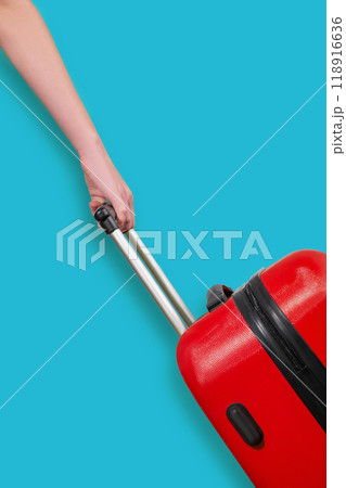 A hand holds a red suitcase on a blue background. Travel concept. 118916636