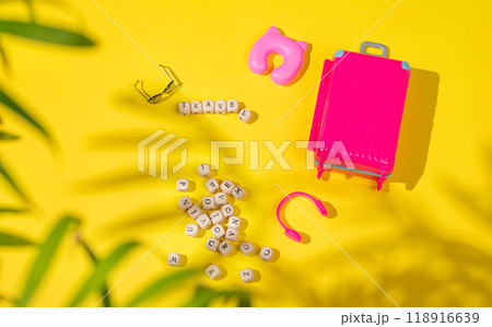 Flat lay pink toy suitcase with travel accessories on a yellow background with shadow. Flat lay pink toy suitcase with travel accessories on a yellow background with shadow. 118916639