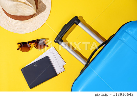 Flat lay blue suitcase with travel accessories, hat and sunglasses on a yellow background. Flat lay blue suitcase with travel accessories, hat and sunglasses on a yellow background. 118916642