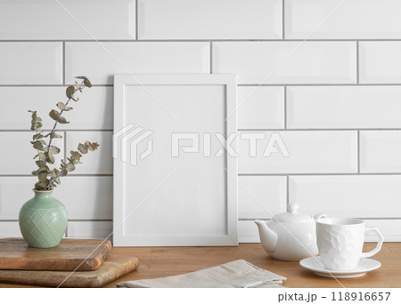 A  frame with a blank canvas against a white tile wall and on a wooden tabletop 118916657