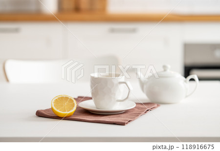 A cup of tea with lemon and a teapot on a white table. Kitchen with wooden empty countertop A cup of tea with lemon and a teapot on a white table. Kitchen with wooden empty countertop 118916675