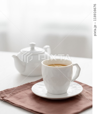 A cup of tea with lemon and a teapot on a white table against the background of a kitchen window. 118916676