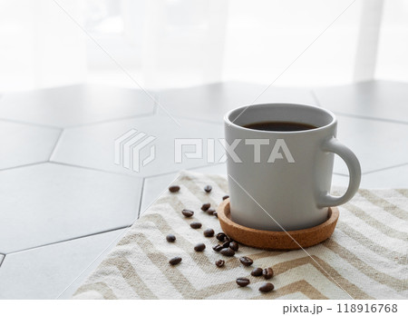 A cup of black coffee on a napkin on a trendy gray tile background with coffee beans A cup of black coffee on a napkin on a trendy gray tile background with coffee beans 118916768