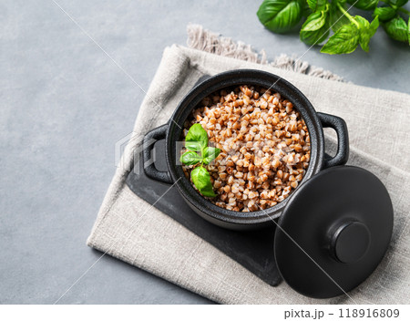 Buckwheat porridge in a black pan on a napkin on a light background with fresh herbs. 118916809