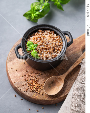Buckwheat porridge in a black pan on a cutting board on a  light background with raw grains, spoon  118916815