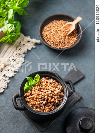 Buckwheat porridge in a black pan on a dark  background with raw grains and herbs. 118916824