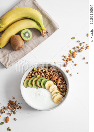 Granola and milk product with banana and kiwi on a white table. 118916864