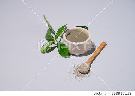 Spa treatment. Blue clay in a bowl and spoon on a light background with leaves and shadow. Spa treatment. Blue clay in a bowl and spoon on a light background with leaves and shadow. 118917112